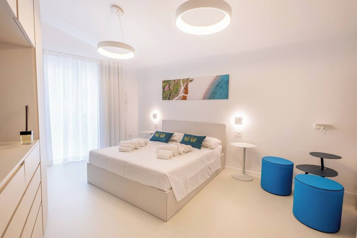 A modern hotel room with a large bed, bedside tables, a painting on the wall, and a view of the outdoors.