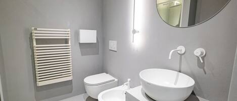 A modern bathroom with a round sink, a toilet, a towel rack, and a mirror.