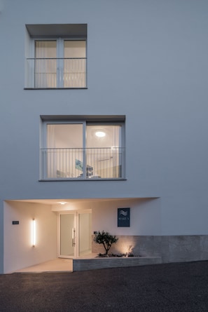 A building with a flat facade, a balcony with metal railings, a glass door entrance, and a small sign with a logo.