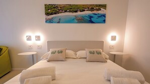 Habitación de hotel con una cama, dos mesitas de noche, una silla verde y un cuadro de una playa.