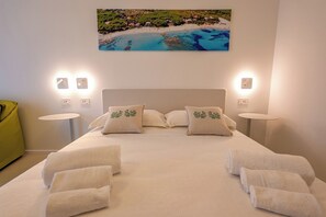 A hotel room with a bed, two bedside tables, a green chair, and a painting of a beach. - Marea Boutique Hotel (Orosei)
