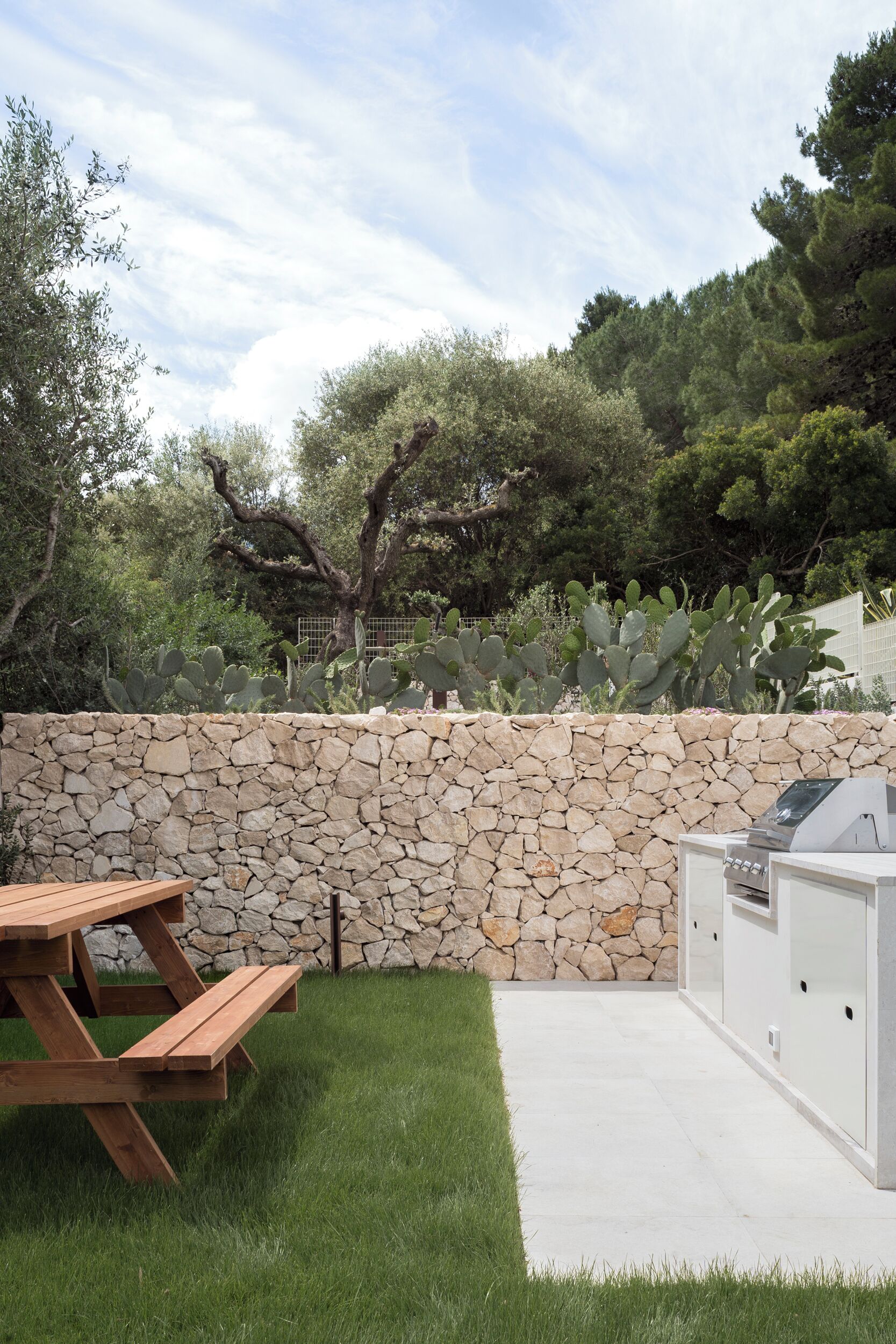 A stone wall, a wooden picnic table, and an outdoor grill area.