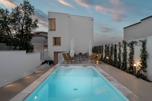 A swimming pool with lounge chairs and a table, surrounded by a white building and greenery. - Marea Boutique Hotel (Orosei)