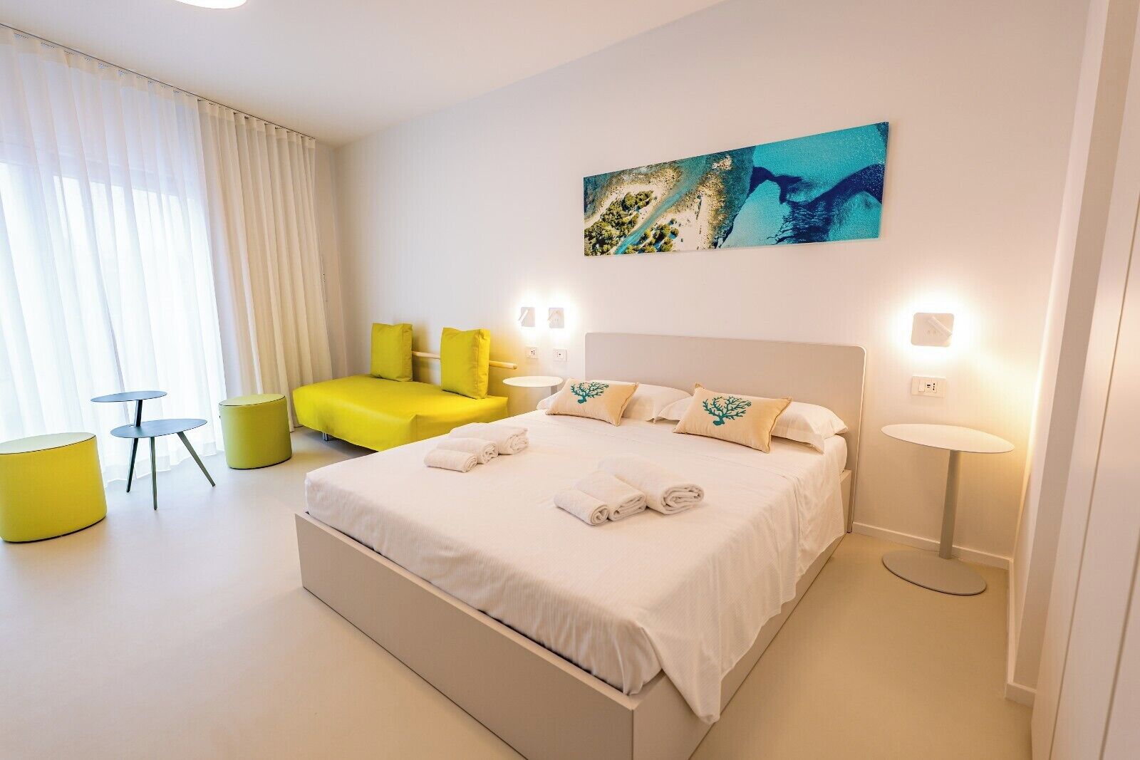 Une chambre d’hôtel moderne avec un grand lit, un canapé, deux petites tables et un tableau au mur.