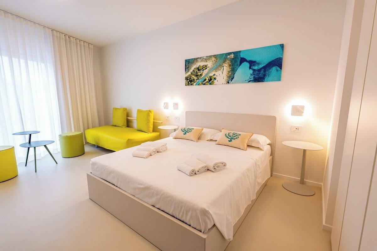 A modern hotel room with a large bed, a small sofa, two round tables, and a painting on the wall.
