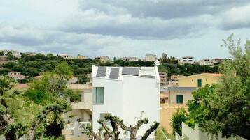 Un barrio residencial con un edificio moderno blanco, vegetación verde y un cielo nublado.