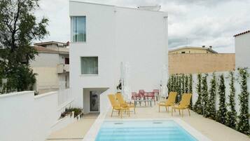 A modern building with a swimming pool, outdoor seating, and a white exterior.