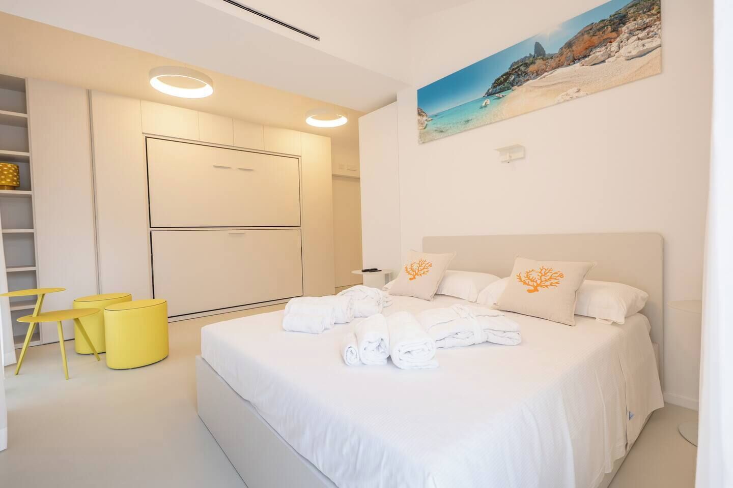 Una habitación de hotel con una cama, un cuadro de una playa y una silla amarilla.