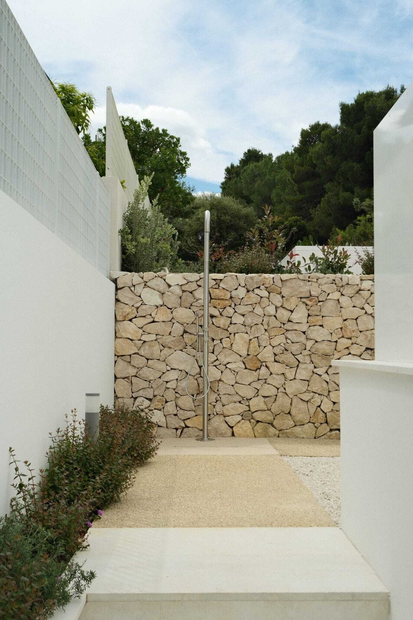 Ein moderner Eingangsbereich im Freien mit einer Steinmauer, einem Metallgitter und einem Betonweg, der zu einem Gebäude führt.
