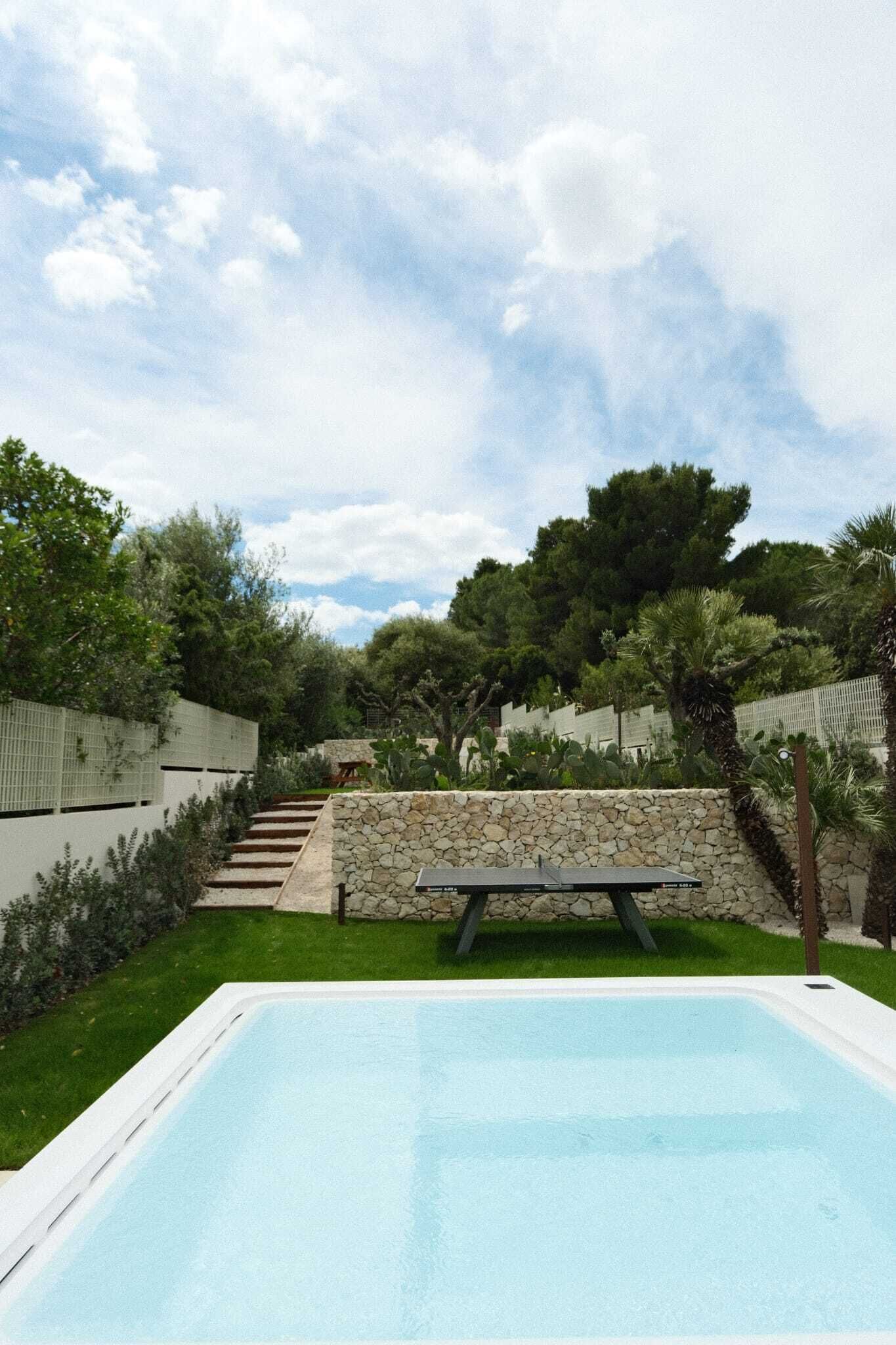 A swimming pool with a stone wall and steps leading up to a patio area.