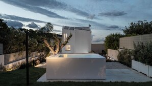 Un edificio moderno con techo plano, piscina rectangular y jardín bien cuidado.