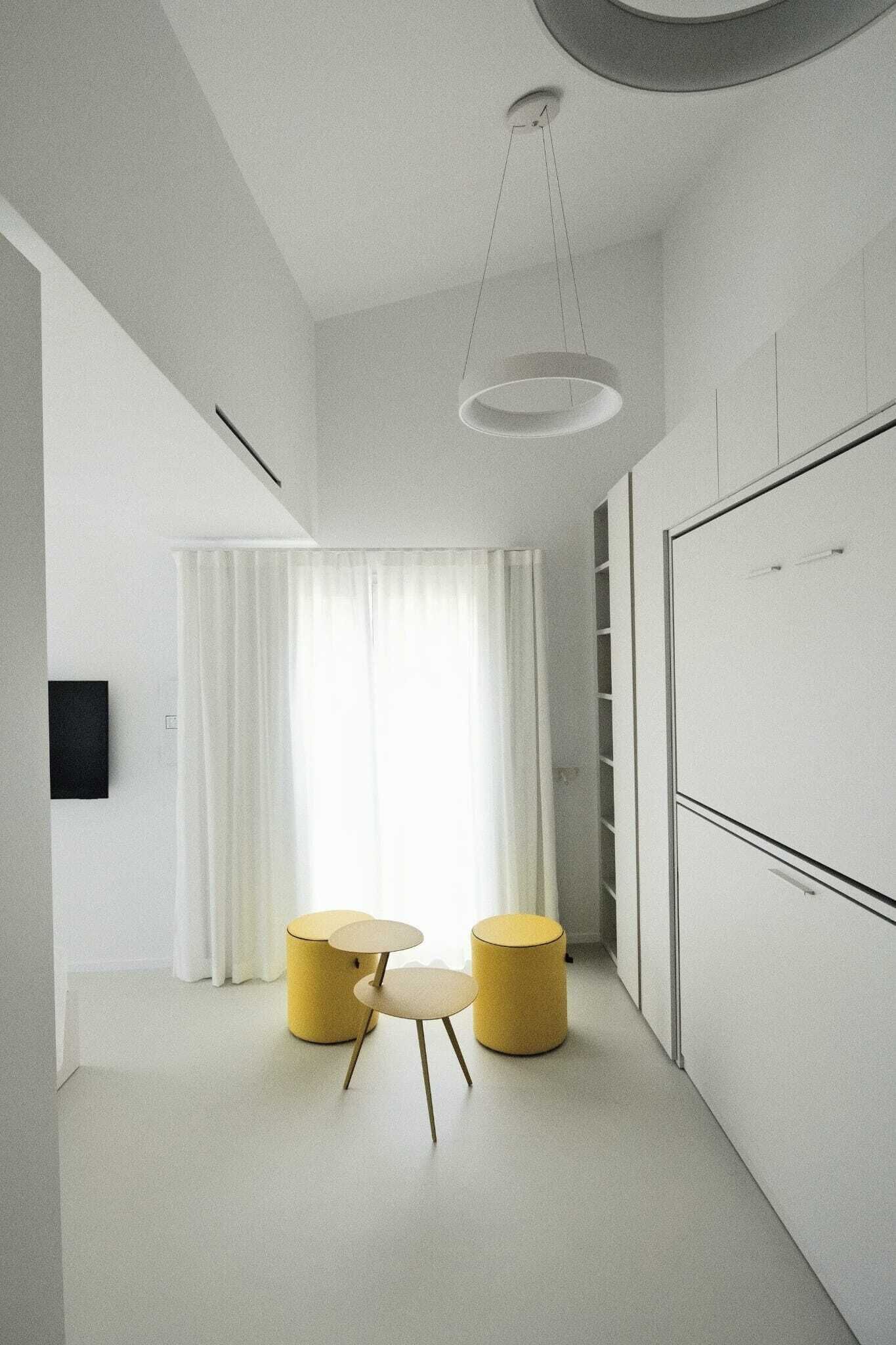Una habitación moderna y minimalista con techo blanco, una lámpara colgante, un armario blanco y una pequeña mesa redonda con dos sillas.