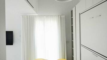 Una habitación moderna y minimalista con techo blanco, una lámpara colgante, un armario blanco y una pequeña mesa redonda con dos sillas.