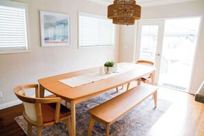 A dining area with a wooden table, chairs, a bench, a hanging light fixture, and a rug. - The Sea Glass  | Coastal Luxury | Close to Beach (San Diego)