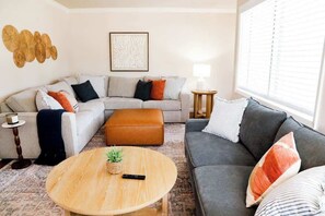 Ein Wohnzimmer mit Ecksofa, rundem Couchtisch und einem Beistelltisch mit Lampe.