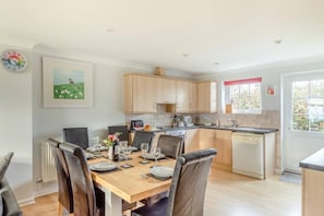 A modern kitchen with wooden cabinets, a dining table set for four, and a view of the outdoors through a window. - 4 bed Lodge Newquay Cornwall Holiday Park Sleeps 8 (Newquay)