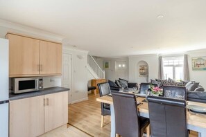 A modern kitchen with wooden cabinets, a microwave, and a dining area with a table and chairs. - 4 bed Lodge Newquay Cornwall Holiday Park Sleeps 8 (Newquay)