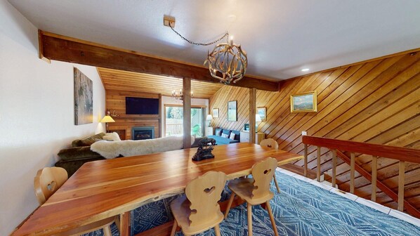 A wooden interior with a dining table, chairs, a chandelier, and a staircase.