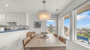 Eine moderne Küche mit weißen Schränken, einem Holzes Esstisch und einem großen Fenster mit Blick auf die Nachbarschaft.