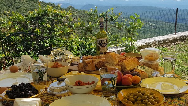 A table set outdoors with food and drinks, overlooking a mountainous landscape. - Le logis - Authentic house with garden and view (Mons)
