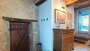 A rustic room with a stone wall, wooden door, and a wooden dresser with a mirror and framed picture. - Le logis - Authentic house with garden and view (Mons)