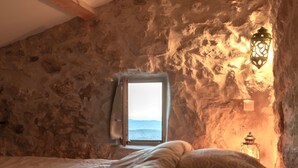 A bedroom with a stone wall, a window, a bed, and a wall-mounted lantern. - Le logis - Authentic house with garden and view (Mons)