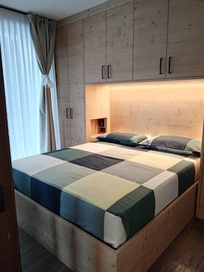 Un lit en bois avec une courtepointe, une tête de lit dotée d’un éclairage intégré et une petite étagère.