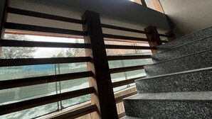 Una escalera con barandas de madera y peldaños de granito que conduce a una habitación con ventanas amplias.