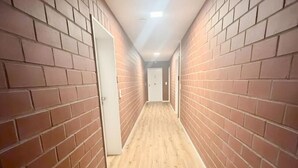 A narrow hallway with brick walls and wooden flooring, leading to a door at the end.