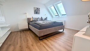 A bedroom with a bed, a desk, a chair, a window, and a radiator.