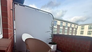 A balcony with a white chair, a potted plant, and a whiteboard.