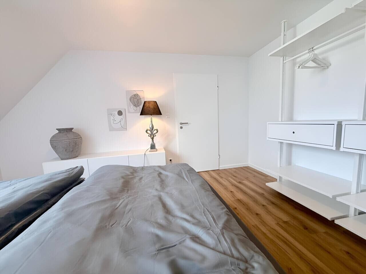 A bedroom with a bed, bedside table, lamp, and a white wardrobe.