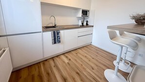 A modern kitchen with white cabinets, a wooden countertop, a microwave, and a bar stool. - City-Loft Lingen Apartment 3 in the heart of Lingen (Lingen (Ems))