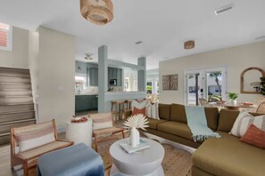 Ein geräumiger Wohnbereich mit einer Couch, Sesseln, einem Couchtisch und einer Küche im Hintergrund.