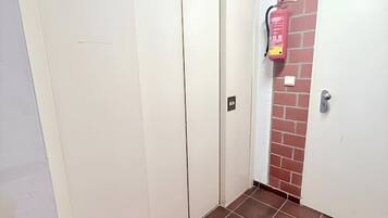 Ein Flur mit an der Wand befestigtem Feuerlöscher, einer Tür und einem gefliesten Boden.