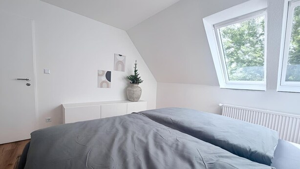 A bedroom with a bed, a white dresser, a potted plant, and a window with a view of trees. - City-Loft Lingen Apartment 1 in the heart of Lingen (Lingen)