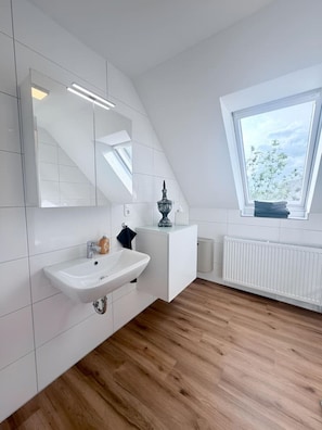 A modern bathroom with a white sink, mirror, and tiled walls. - City-Loft Lingen Apartment 1 in the heart of Lingen (Lingen)