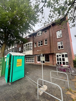 A brick building with a green portable toilet, a bicycle, and a metal fence. - City-Loft Lingen Apartment 1 in the heart of Lingen (Lingen)
