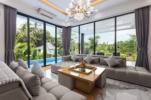 Una sala de estar moderna con un amplio sofá modular, una mesa de centro de vidrio y vistas a una piscina y vegetación.