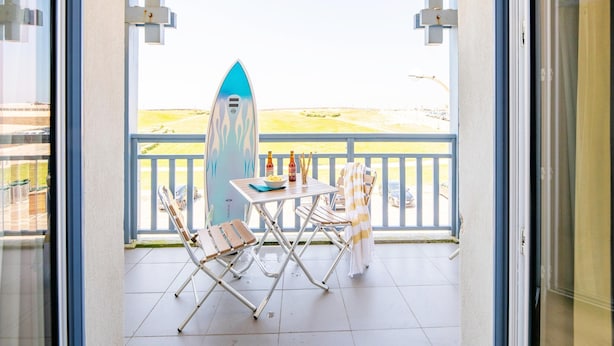 Un balcón con una tabla de surf, dos sillas, una mesa y botellas.