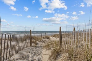 A sandy beach path with wooden fencing leading to the ocean. - Beachfront Bliss | Ocean Views + Family-Friendly Yard (Emerald Isle)