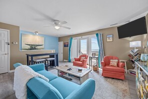 A living room with a ceiling fan, a TV, a painting, a coffee table, and two chairs. - Beachfront Bliss | Ocean Views + Family-Friendly Yard (Emerald Isle)