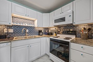 A modern kitchen with white cabinets, a black and blue backsplash, a built-in microwave, and a stove. - Beachfront Bliss | Ocean Views + Family-Friendly Yard (Emerald Isle)