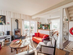 A cozy living room with a fireplace, a sofa, a dining table, and a kitchen area visible through a sliding door. - Cozy Holiday Home Near the sea (Porspoder)
