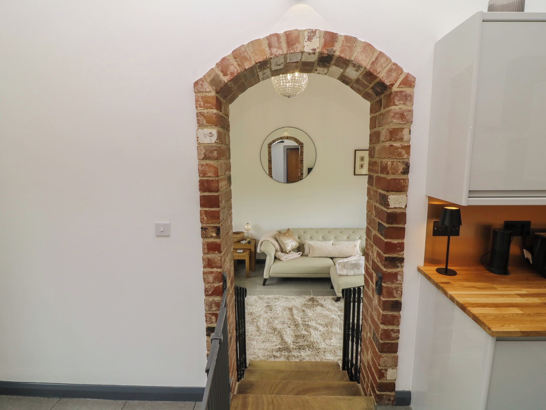 A staircase leading to a living area with a brick archway, a round mirror, a sofa, and a lamp.