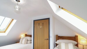 Un dormitorio con dos camas, un tragaluz, una puerta de madera y una lámpara en el techo.