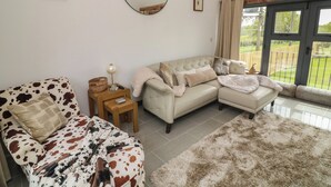 Una sala de estar con un sofá, un sillón estampado, una mesita con una lámpara y un espejo grande en la pared.