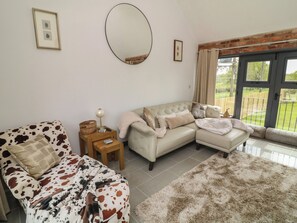 A living room with a sofa, a patterned armchair, a small table with a lamp, and a large mirror on the wall. - The Croft, Home Farm (Ripley)