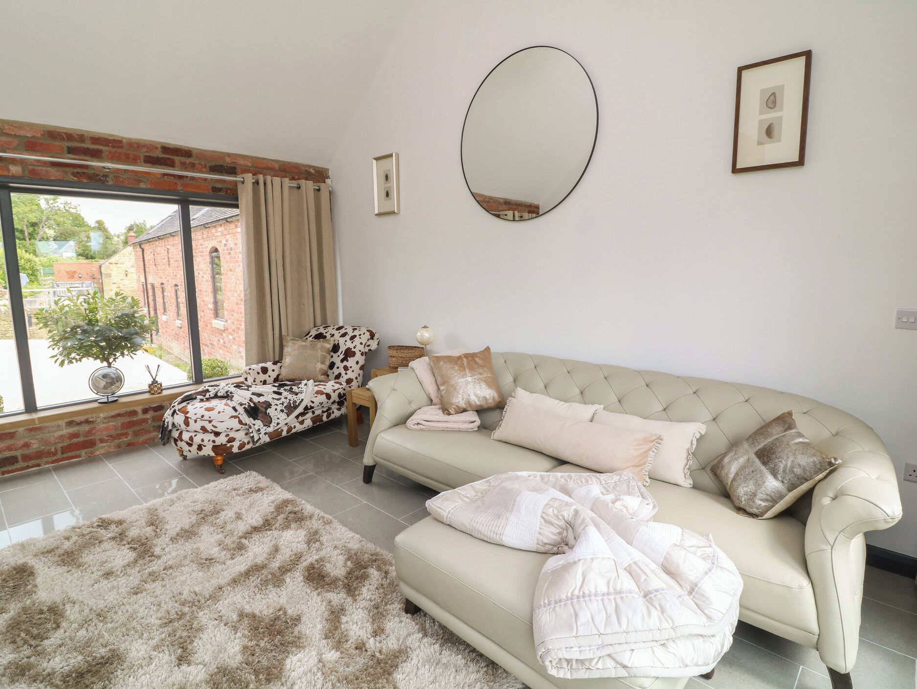 A living room with a sofa, a patterned armchair, a rug, a mirror, and a framed picture on the wall.