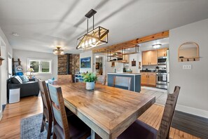 Eine moderne Küche mit Holzbalken, ein Essbereich mit einem Holztisch und ein Wohnzimmer mit einer Couch und einer Steinwand.